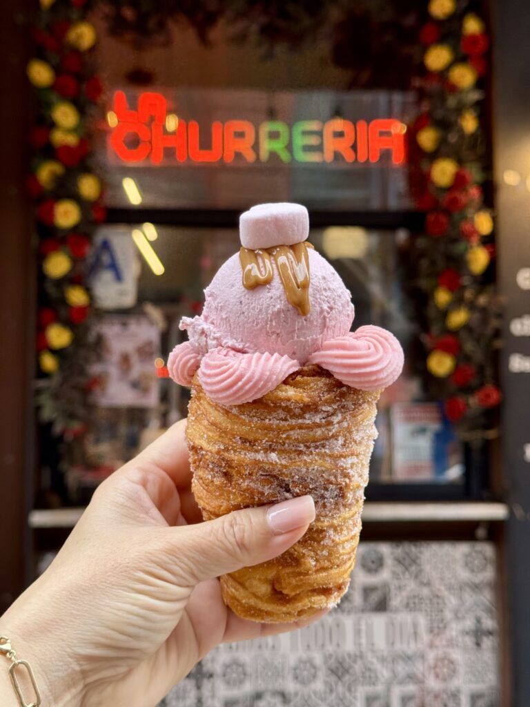 A hand holding a churro-based dessert topped with ice cream.